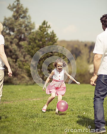 Daughter kicking ball to father and mother in park