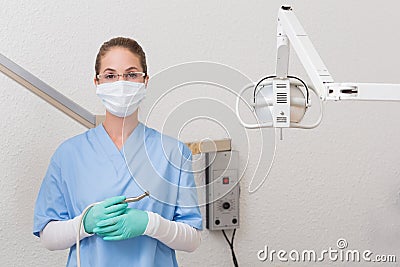 Dentist in blue scrubs holding dental drill looking at camera