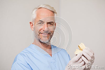 Dentist in blue scrubs holding mouth model