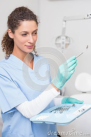 Dentist in blue scrubs holding tray of tools