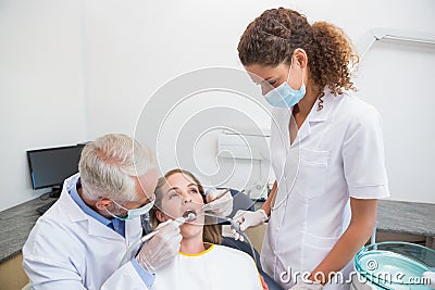 Dentist examining a patients teeth in the dentists chair with assistant
