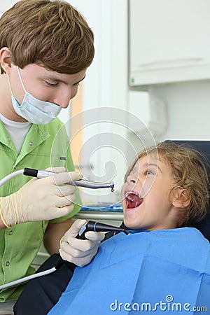 Dentist holds grinding drill, girl opens mouth