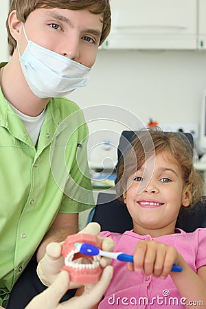 Dentist shows to patient girl how to brush teeth