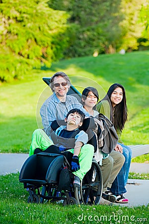 Disabled boy in wheelchair with family outdoors on sunny day sit