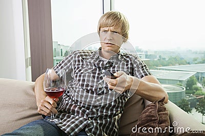 Displeased mid-adult man with wine glass watching television on sofa at home