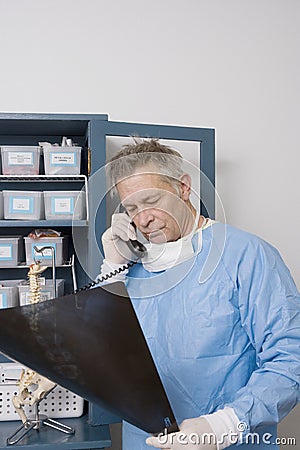 Doctor Analyzing X-Ray Report While Using Landline Phone