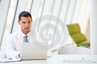 Doctor Using Laptop Sitting At Desk In Modern Hospital