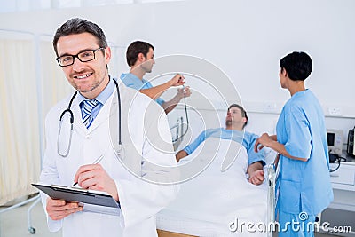 Doctor writing reports with patient and surgeons in background