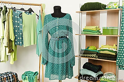 Dressing closet with green clothes arranged on hangers and shelf, dress on a mannequin.