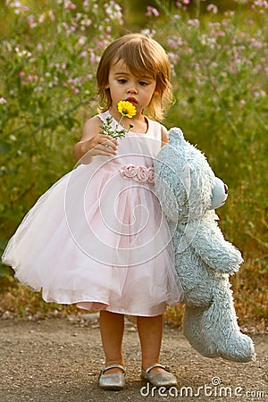 Dressy two-year-old girl in pink dress holding stuffed bear and flower