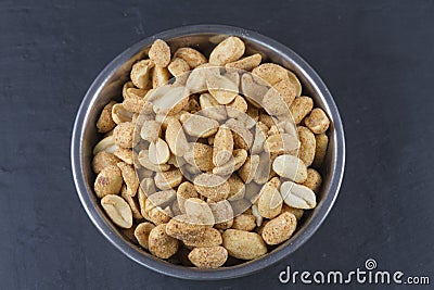 Dry roasted peanuts in metal bowl on slate.