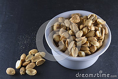 Dry roasted peanuts in white ramekin on slate