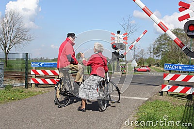 Elderly couple on bikes waits at railway crossing