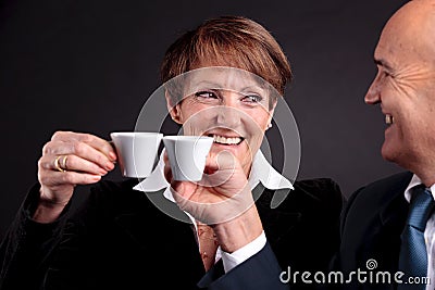 An elderly couple holding up two cups of espreso coffee