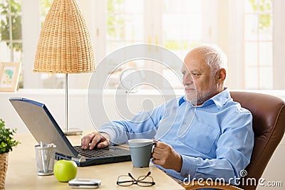 Elderly man using computer, having coffee
