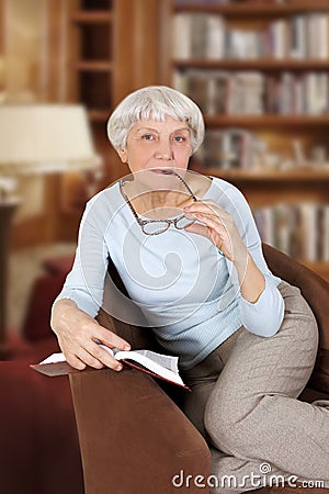 Elderly woman with book and glasses sitting in a chair