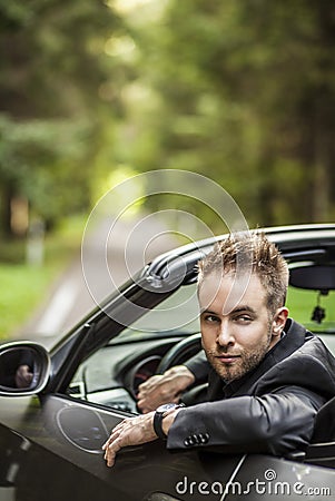 Elegant young happy man in convertible car outdoor.