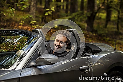 Elegant young happy man in convertible car outdoor.