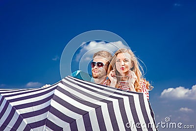 Emotional couple hiding behind the umbrella and having fun on th