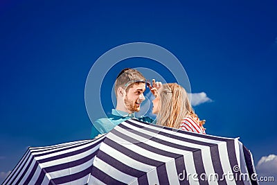 Emotional couple hiding behind the umbrella and having fun on th