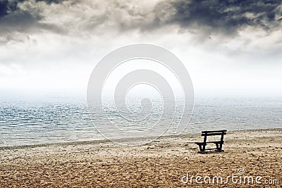 Empty wooden bench on the beach in cloudy weather