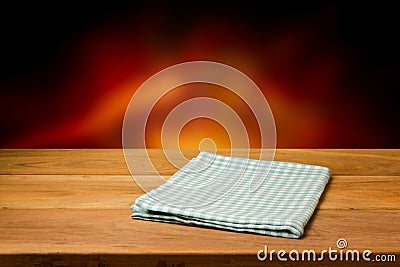 Empty wooden table with checked tablecloth over blur fire background.