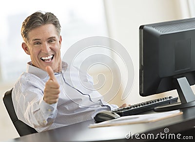 Excited Businessman Gesturing Thumbs Up At Desk