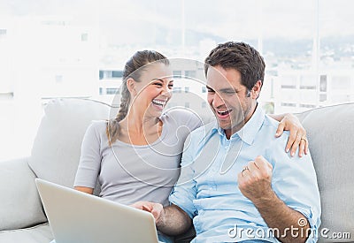 Excited couple sitting on the sofa using laptop together