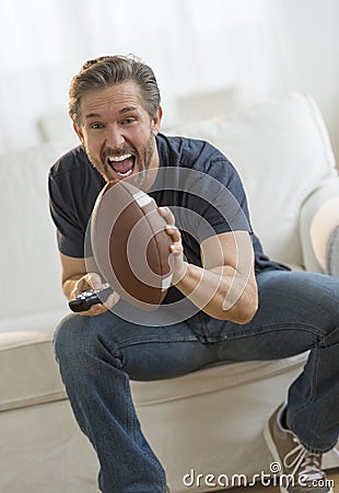 Excited Man Watching American Football Match On Sofa