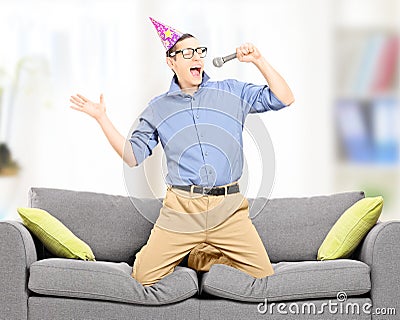 Excited young man with party hat singing on a microphone