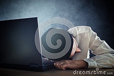 Exhausted man sleeps on laptop at office desk