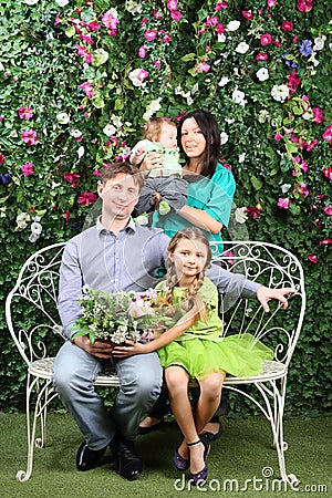 Family of four sit on white bench with bunch of flowers