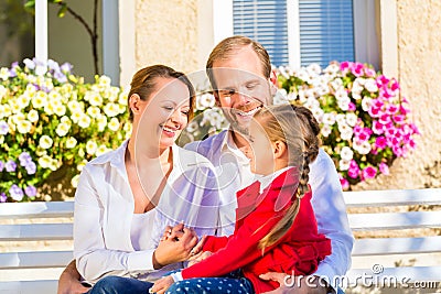 Family on garden bench in front of home