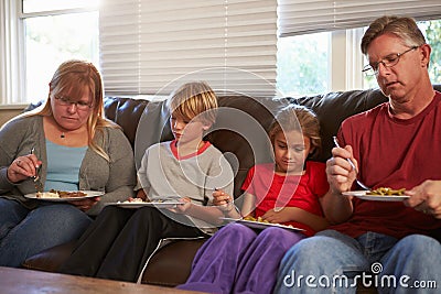 Family With Poor Diet Sitting On Sofa Eating Meal