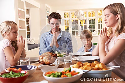 Family Saying Prayer Before Eating Roast Dinner