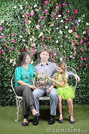 Family sit on white bench with bunch of flowers