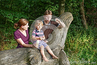 Family of three blowing soap bubbles together in summer forest