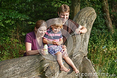 Family of three blowing soap bubbles together in summer forest