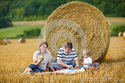 Family of three picnicking on yellow hay field in summer.