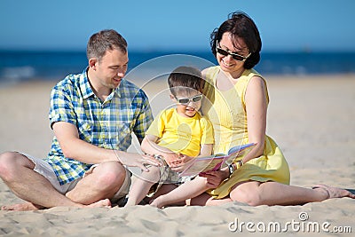 Family of three reading book on beach