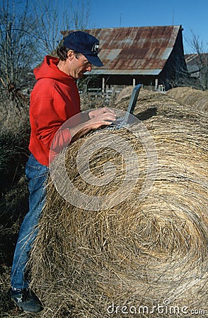Farmer with laptop computer on hay bale
