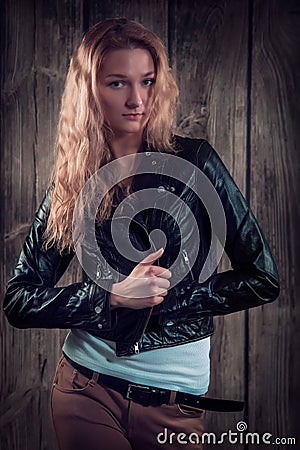 Fashion model with curly hair dressed in black jacket, denim pants and tall boots over wooden wall background