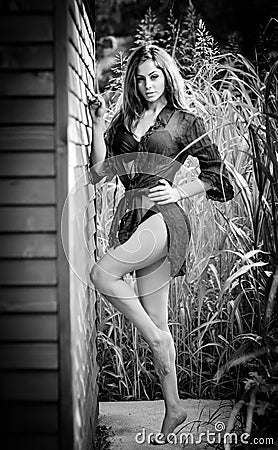 Fashion portrait of sexy brunette in black swimsuit leaning on wooden cabin wall. Sensual attractive woman with long legs