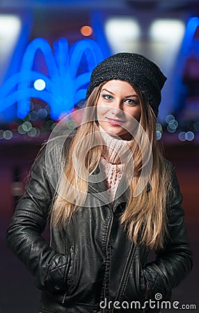 Fashionable lady wearing cap and black jacket outdoor in xmas scenery with blue lights in background. Portrait of young beautiful
