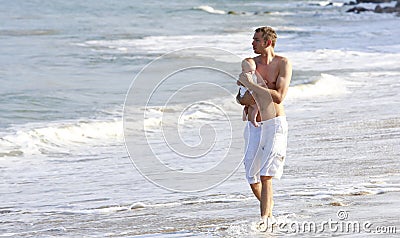 Father and baby walking on the beach with crashing waves