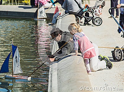 Father and daughter push toy sailboat in fountain in Luxembourg Garden, Paris, France