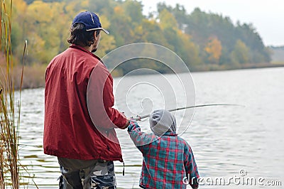 Father and little son fishing together on autumn day backgound