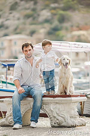 Father and son sits with dogs on a bench near the sea