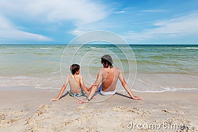 Father and son sitting on the sandy beach.