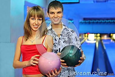 Fellow and girl stand with balls for bowling